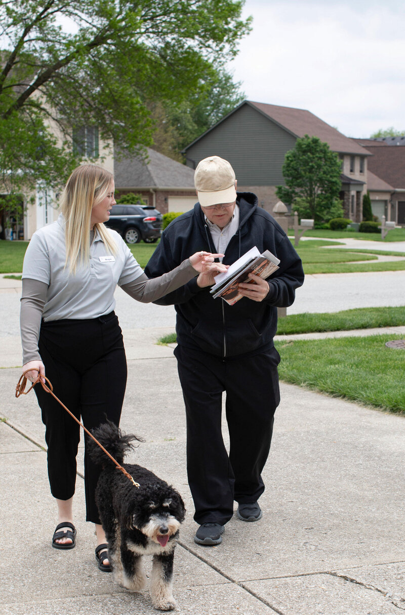 Elderly man smiling while walking to the mailbox with caregiver beside him