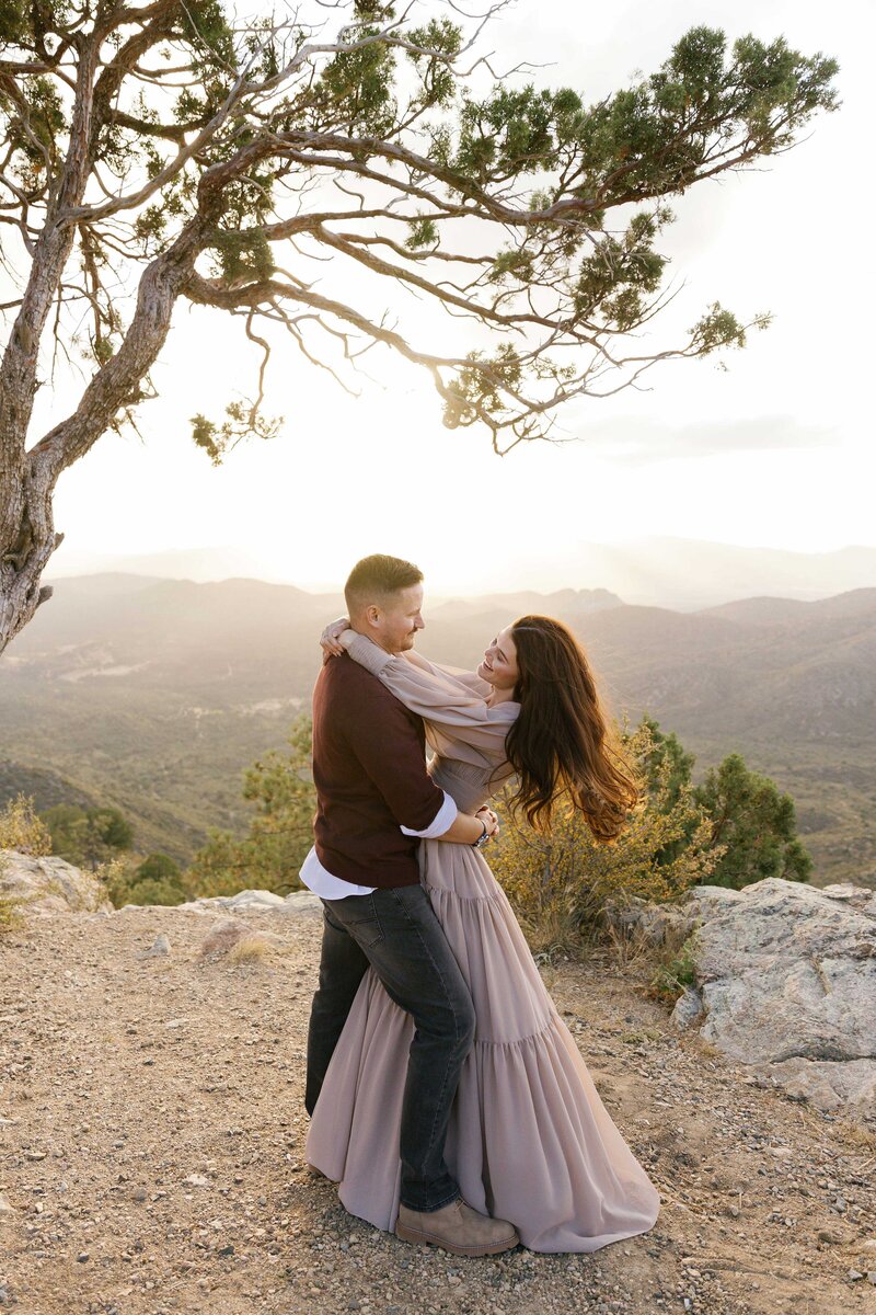 Couple dances together under a tree on the top of a mountain.