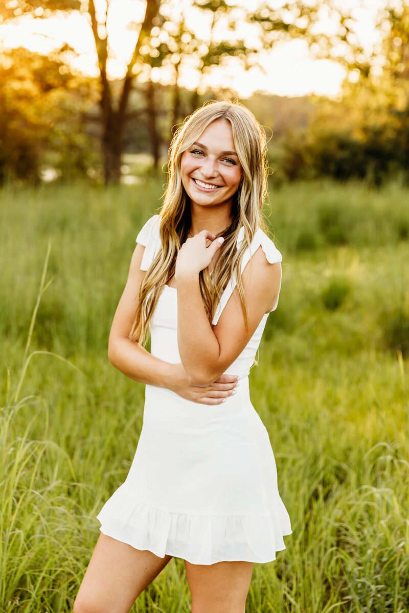 high school teen in white dress standing in a field at sunset near Appleton