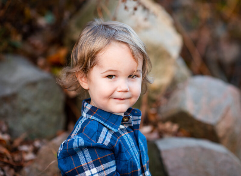 A young child wearing a blue plaid shirt, looking playfully over their shoulder by Leslie Q Photography