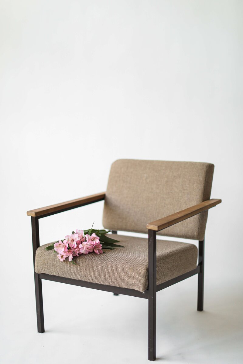 An empty taupe chair with pink flowers on the seat in front of a white background.