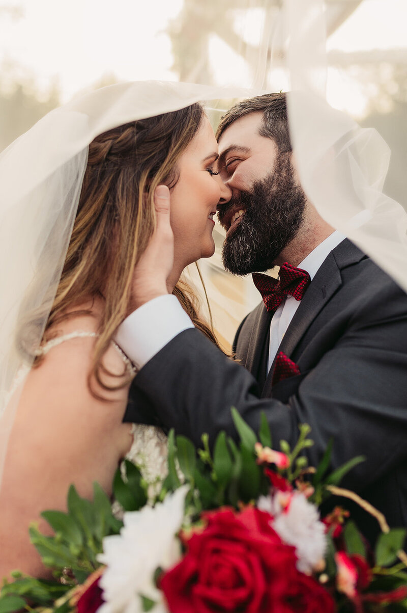 groom pulls bride in for a romantic kiss under wedding veil