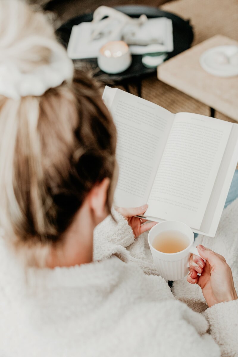 Woman sitting on couch with a book and white mug