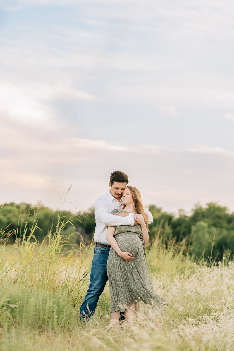 pregnant woman embraces husband in a field