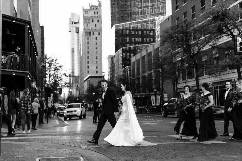 Bride and Groom hold hands and walk across main street in Downtown Fort Worth with Courthouse in the distant back ground