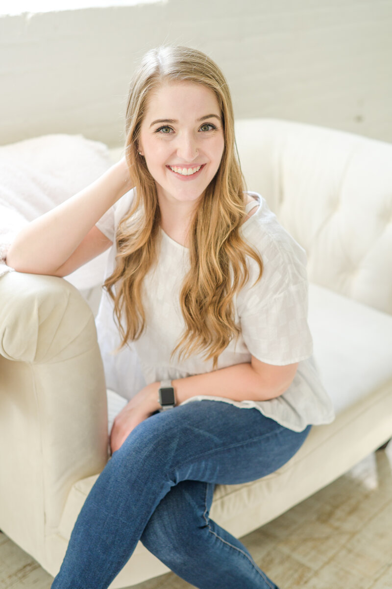 Baltimore Wedding Photographer, Cait Kramer smiles while sitting on cream couch