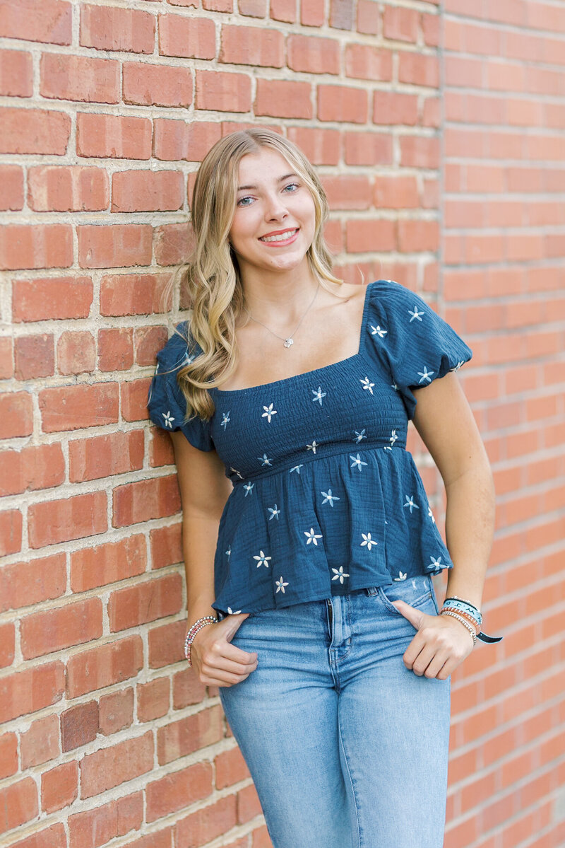 Senior portrait of a smiling teen girl leaning against a brick wall, taken by Raleigh Senior Photographer Lindsey Lambert Photography.