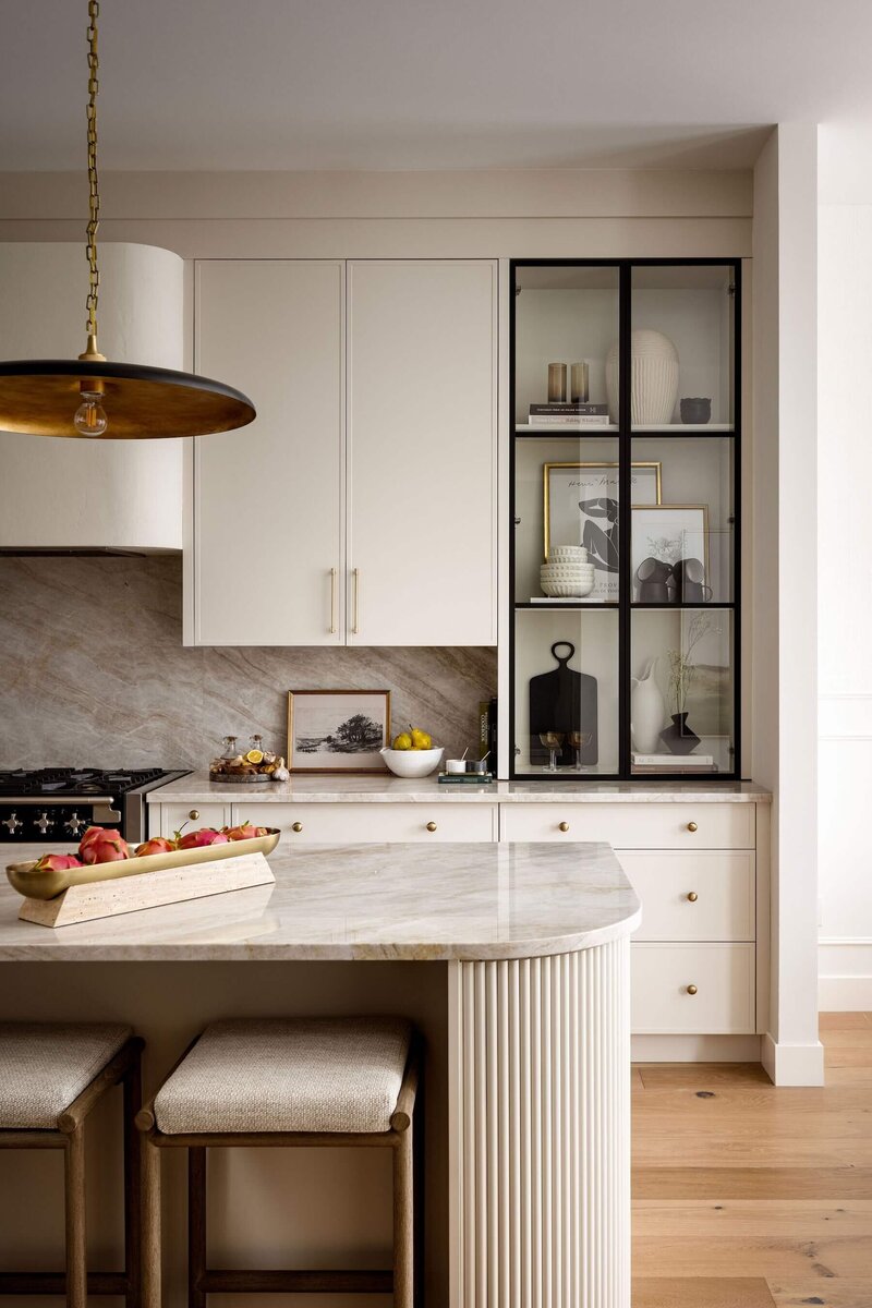 Oval kitchen island with fluted details, plaster hood fan and natural cream cabinets with a glass cabinet feature. 