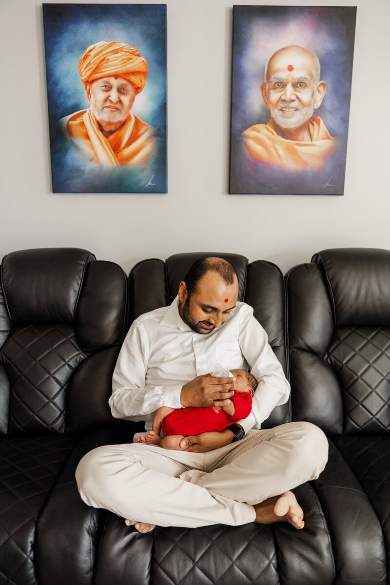 A father giving his newborn son a bottle while sitting on his couch during an in-home newborn session in St. Louis, Missouri. 