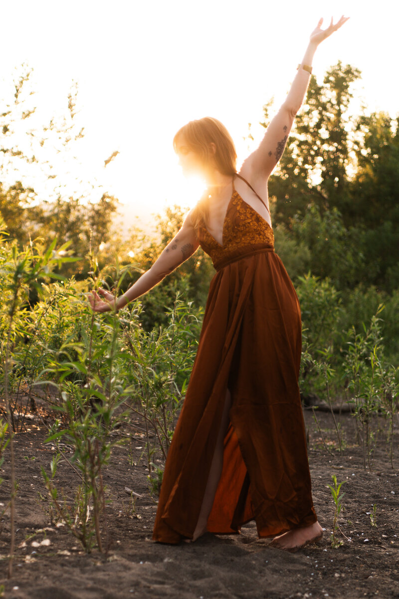 mentor, healer, guide with arms wide in a green field with a sunburst behind her