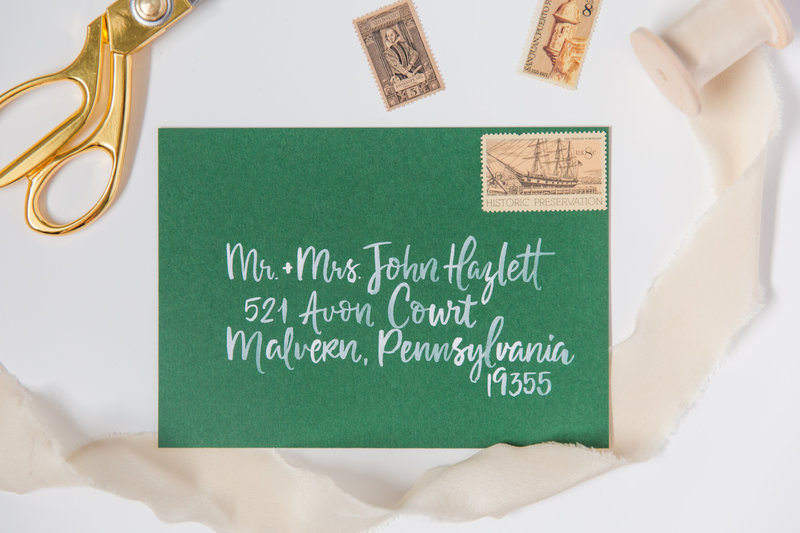 Watercolor calligraphy with white ink on a green envelope  by Katy of Lewes Lettering Co.