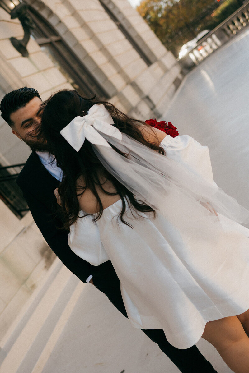 Modern bride in short white dress with bow and red bouquet, candid elopement moment captured by Tarah Shea Photography