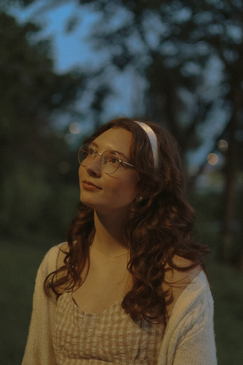 A portrait of a woman not looking at the camera with her head tilted and illuminated by a streetlight.