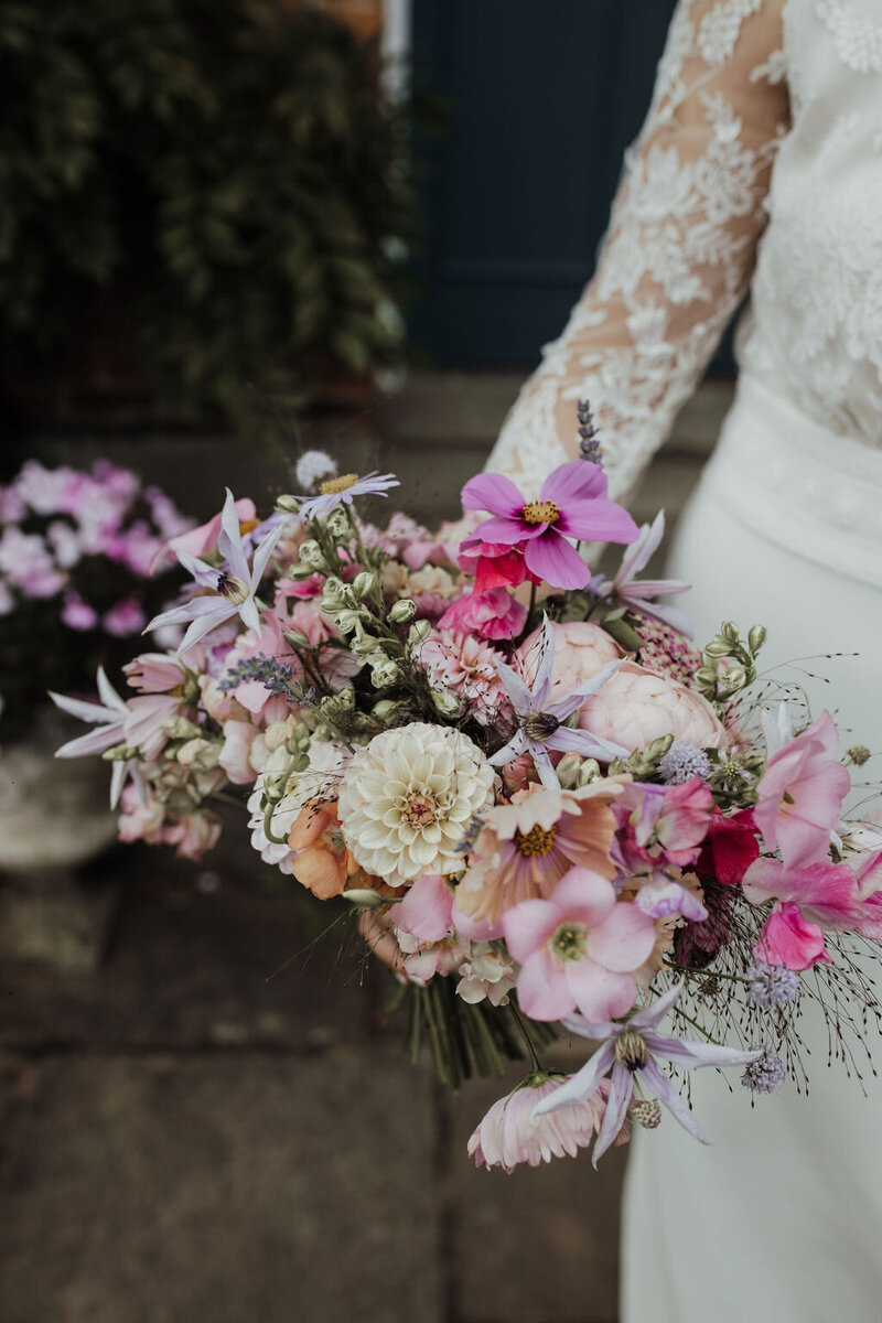 A newly married couple walking along the cliff tops in Cornwall. The bride is carrying a bouquet of purple orchids, yellow crespedia and pink roses