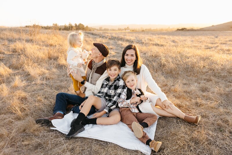family sitting on picnic blanket at crane creek, playing with each other in a field of golden grass