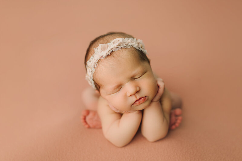 newborn baby in froggy pose on a pink backdrop