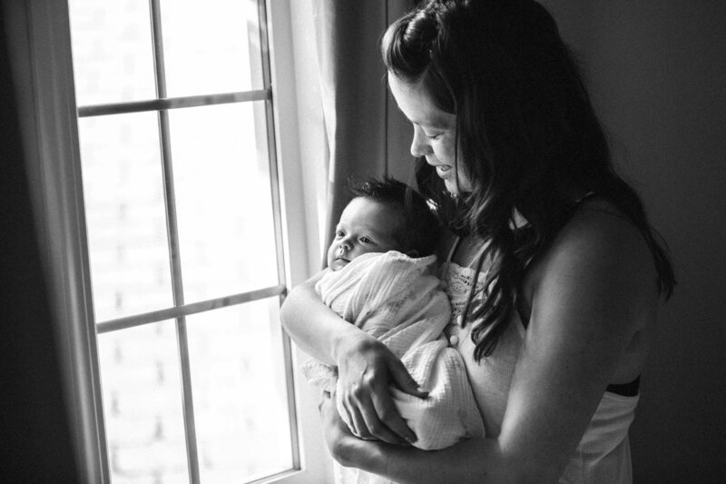 mom holds new baby standing by a window