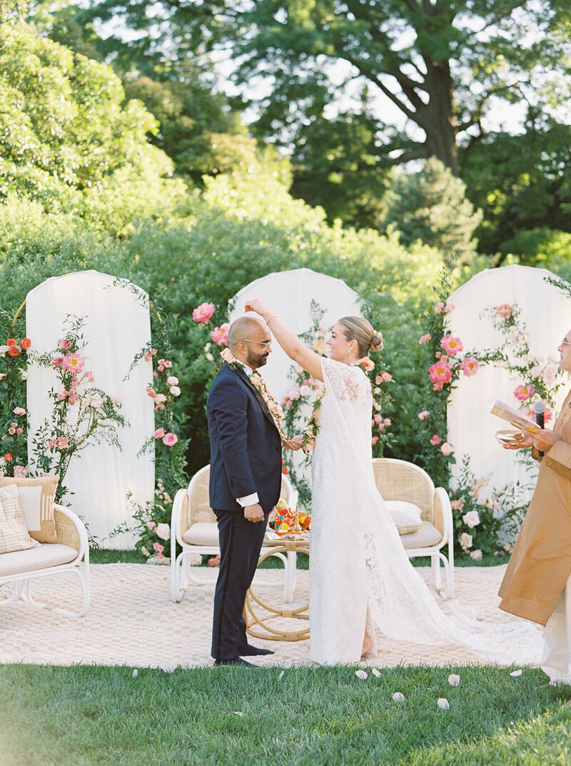 RI Wedding Photographers | A bride and groom exchange vows outdoors, framed by lush greenery and floral arches. 