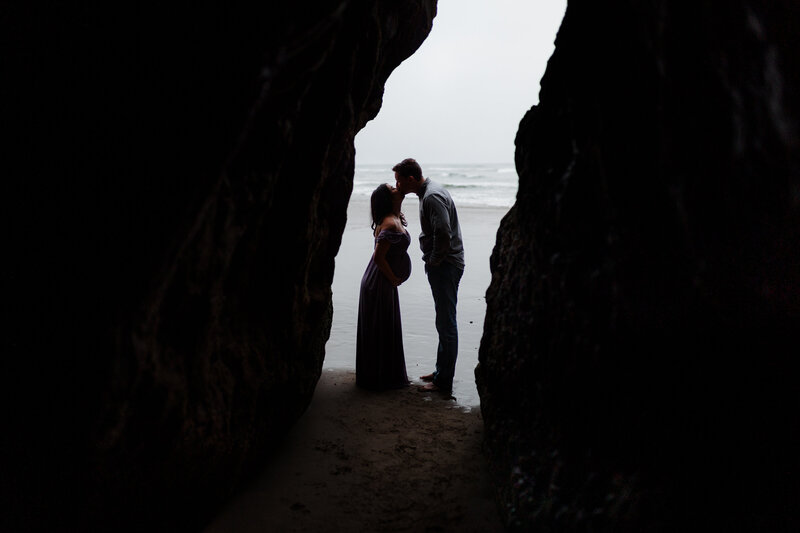 Silhouette of a couple holding hands under a rock arch, captured beautifully by an Oregon Coast Elopement and Wedding Photographer.