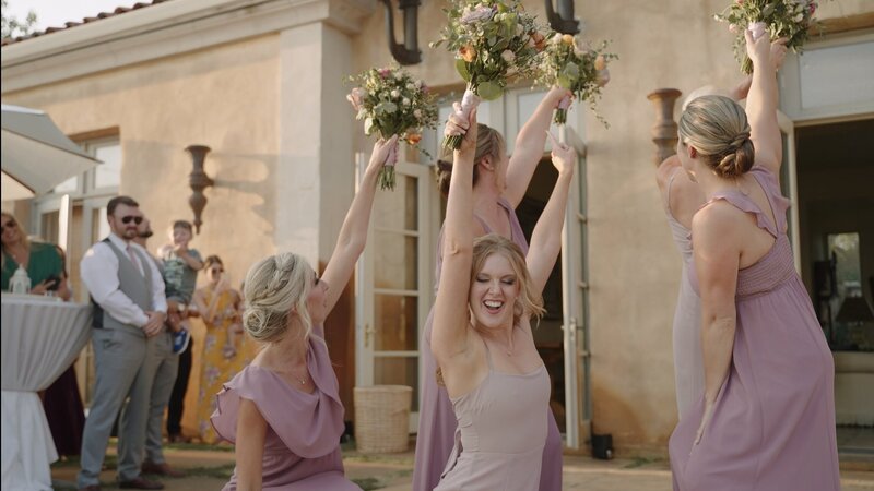 The bridal party is dancing with their flowers and all pointing out second floor balcony for grand entrance of bride and groom  by  Jimmy Shin Film based in Los angeles wedding videography