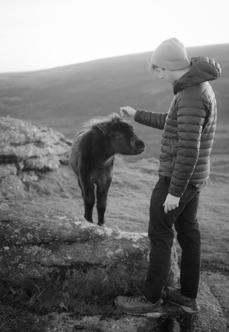 Elliot Govier, a UK based documentary wedding photographer standing next to a pony in Dartmoor
