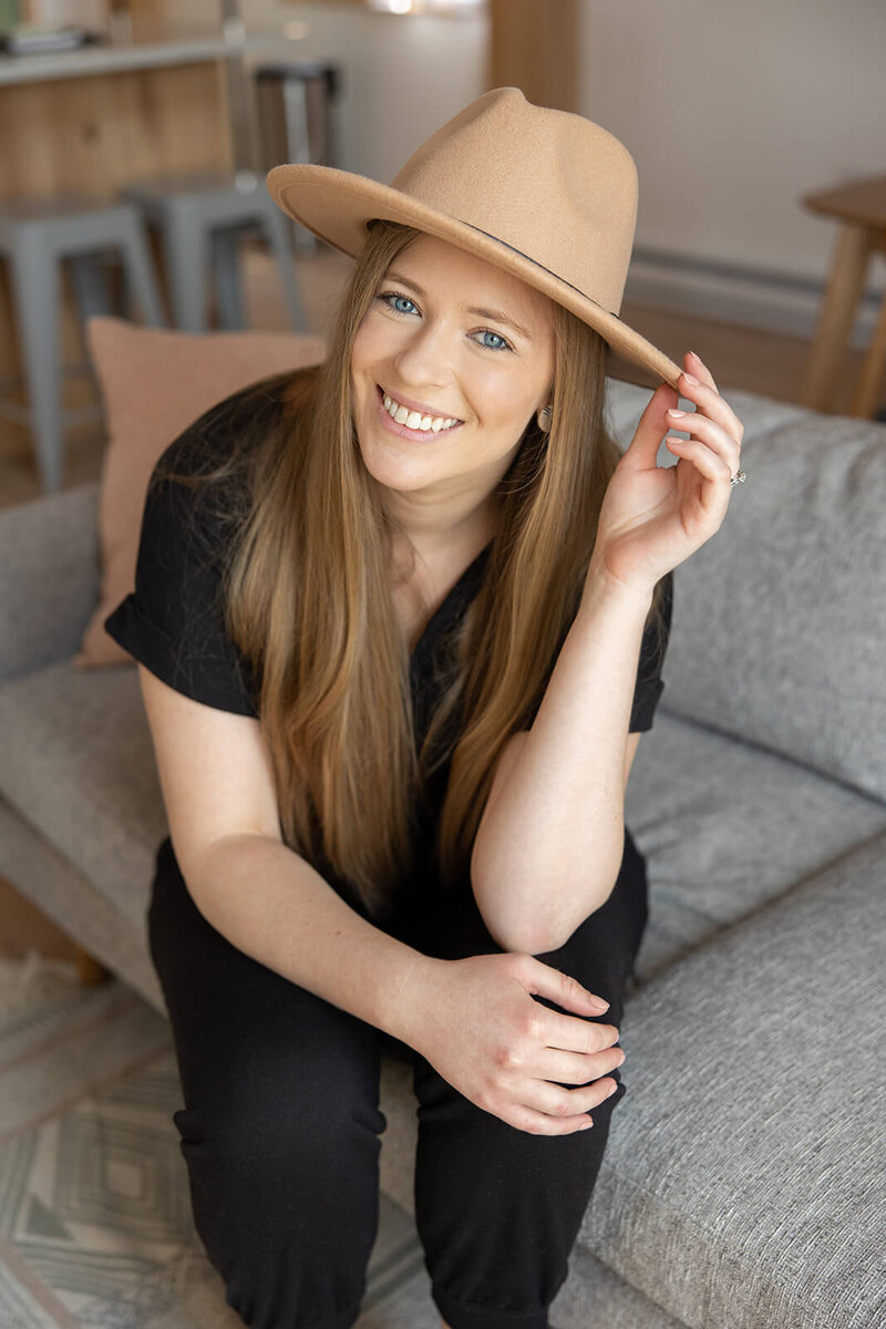 Laurel of Laurel Deane Creative sitting on the couch and smiling while holding a wide brim hat