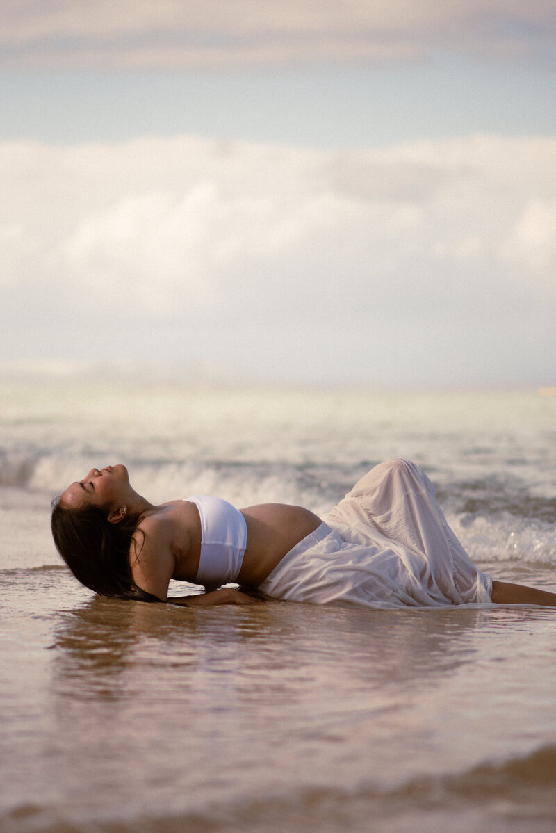 Woman posing on sand at the beach in Oahu, Hawaii for maternity photos