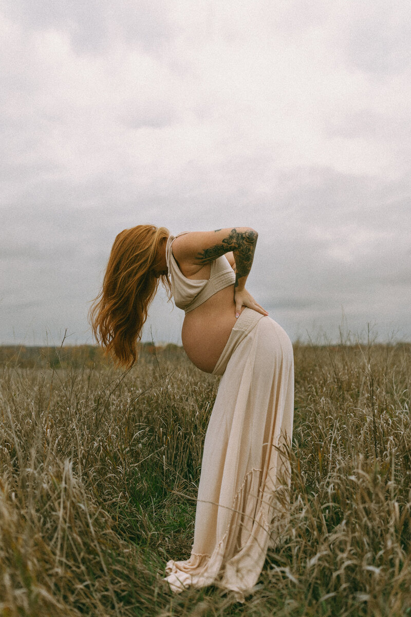 Expecting mother in a two piece outfit in a wheat field on a gloomy day.