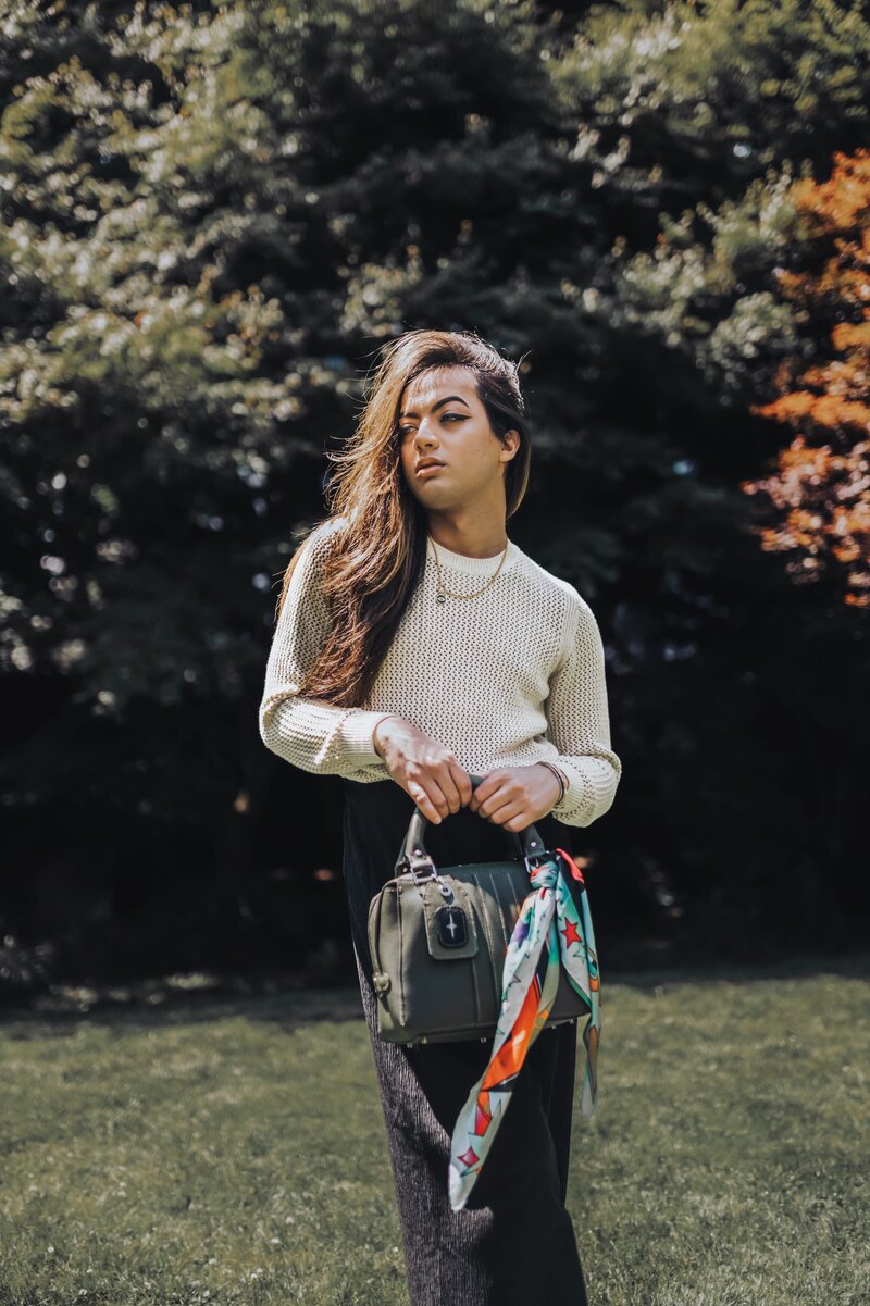 Woman with long brown hair poses in front of trees holding a purse with a colorful scarf tied around the handle.
