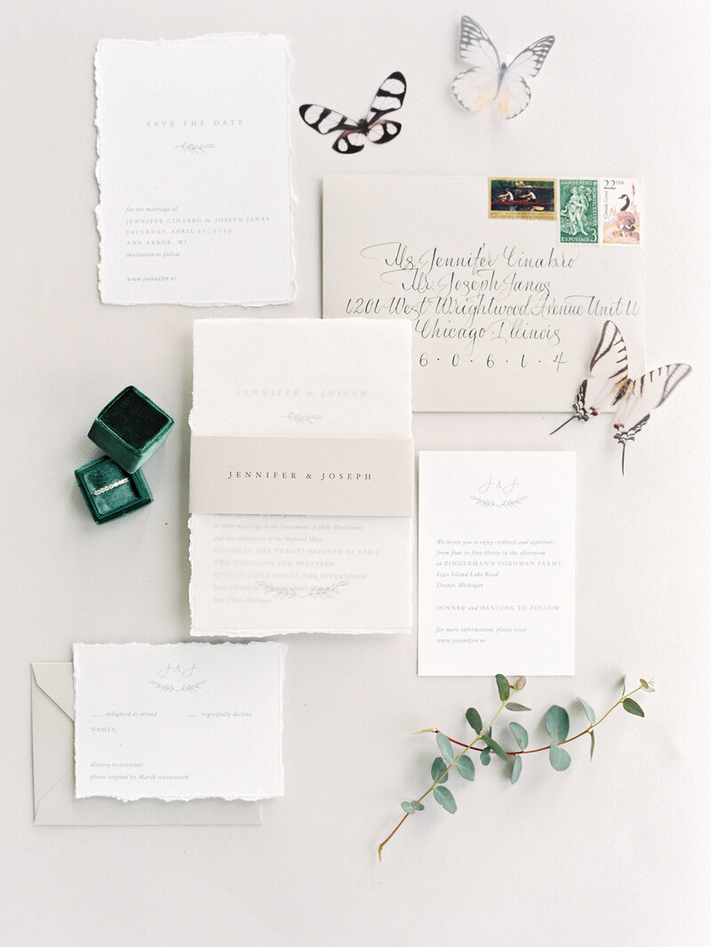 Styled spring flatlay of August & White hand torn invitations with the Mrs. box, wedding ring, & butterflies at Cornman Farms