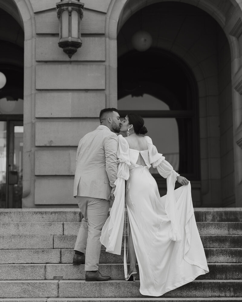 Bride and groom walking up steps of a courthouse after their elopement and kissing