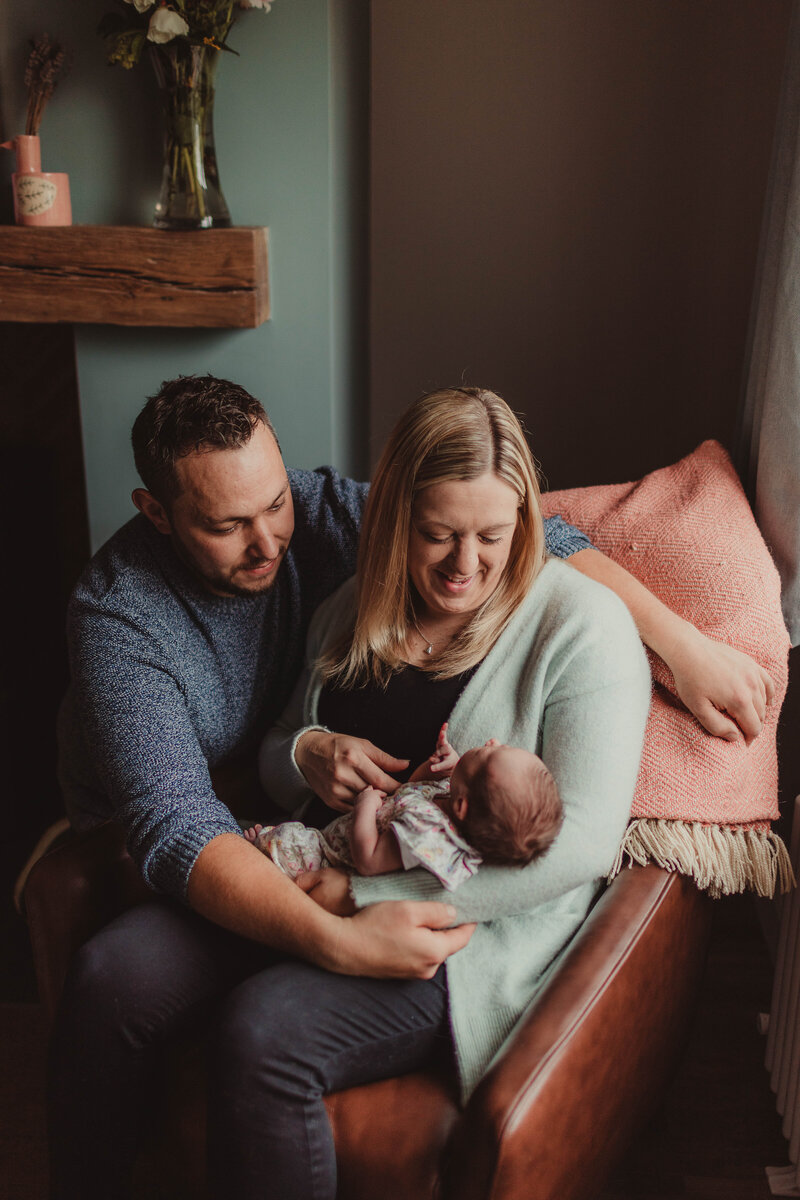 Newborn baby and parents sat on armchair during at home family photoshoot