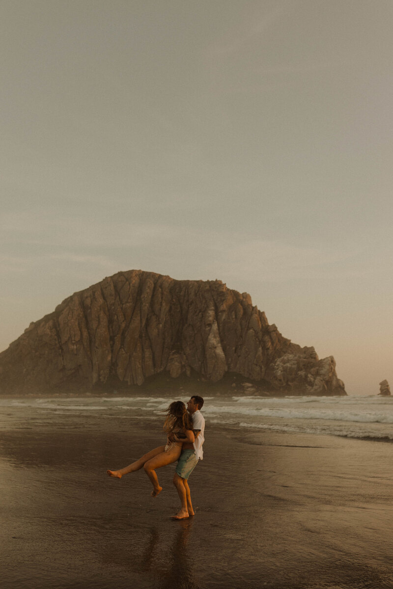 man swinging girl around on the beach