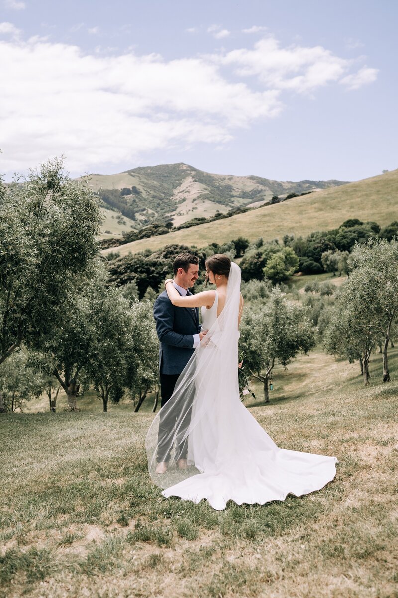 bride and groom in front of olive grove view of mountains in akaroa at mt vernon wedding venue