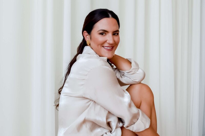 Emily Michele smiling in a beige satin shirt, exuding warmth, confidence, and feminine ease — symbolizing inner peace and self-embodiment through the Unveiled transformation.