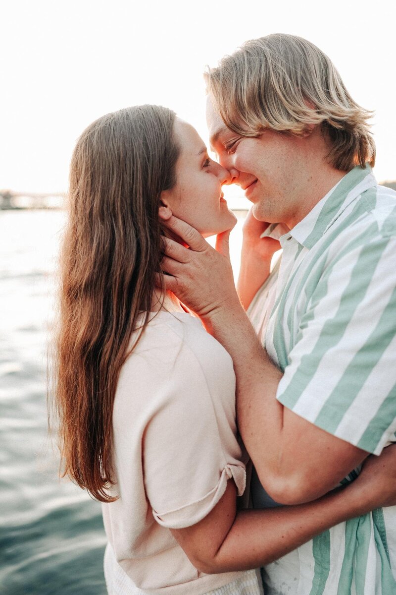 A couple embracing and touching foreheads affectionately by the waterfront at sunset with a Destination Wedding Photographer capturing their love.