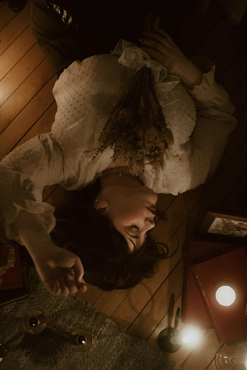 author lays on the floor surrounded by books and candles