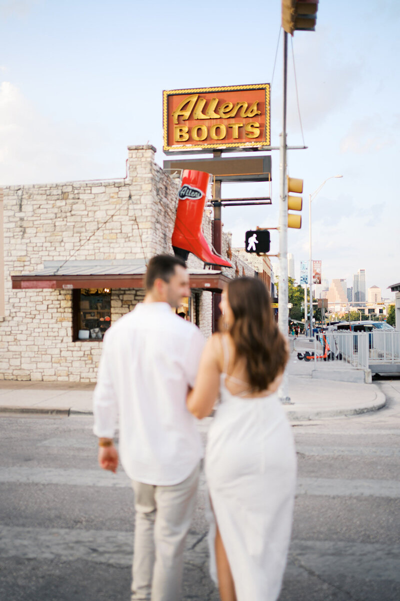 Couple holding hands walking on the street with a boot store in the background