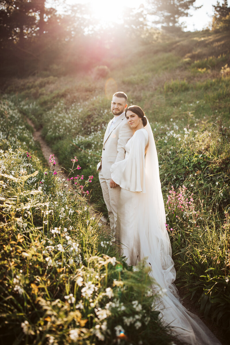 Bride and groom standing together in a wildflower meadow at sunset during their Maine elopement.