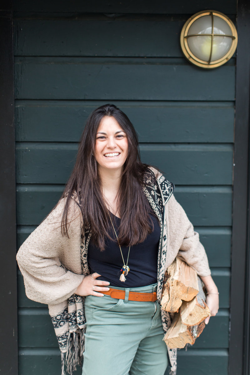 white female brown hair  holding logs in one hand and other hand on hip smiling at camera