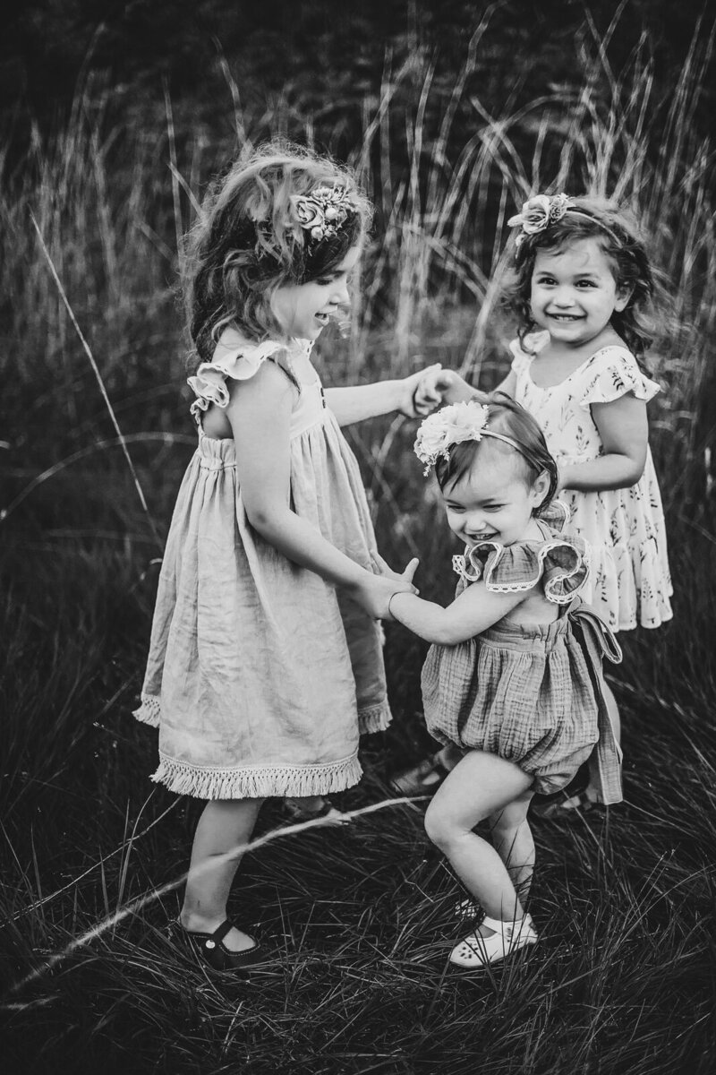 Black and white photo of three sisters playing ring around the rosie during a family session in De Soto, Missouri. 