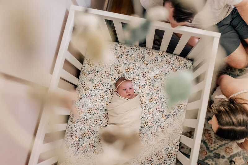 toddler boy in nursery, mobile hanging over crib, looking at baby sister