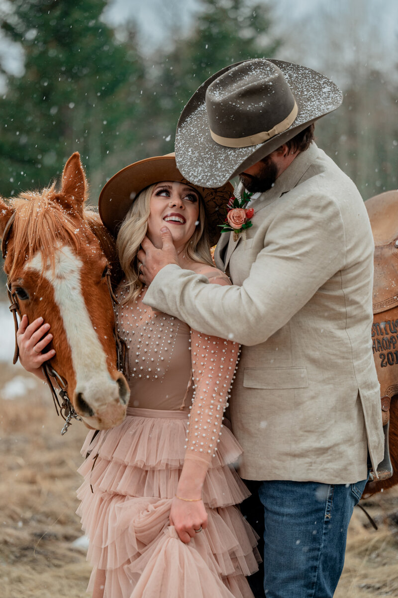 Bride and groom look at each other and almost kiss, with their horse in the background on their wedding day