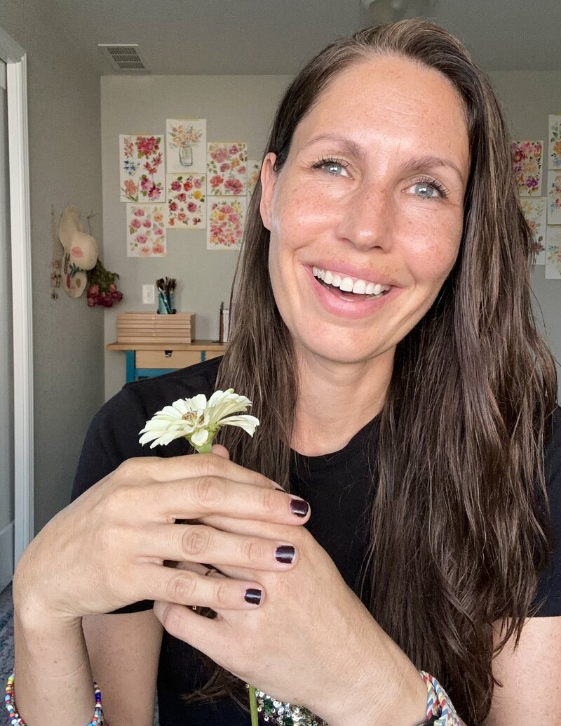 Woman smiling holding a flower and sitting in an art studio