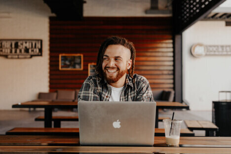 Man smiling while on laptop with a iced coffee
