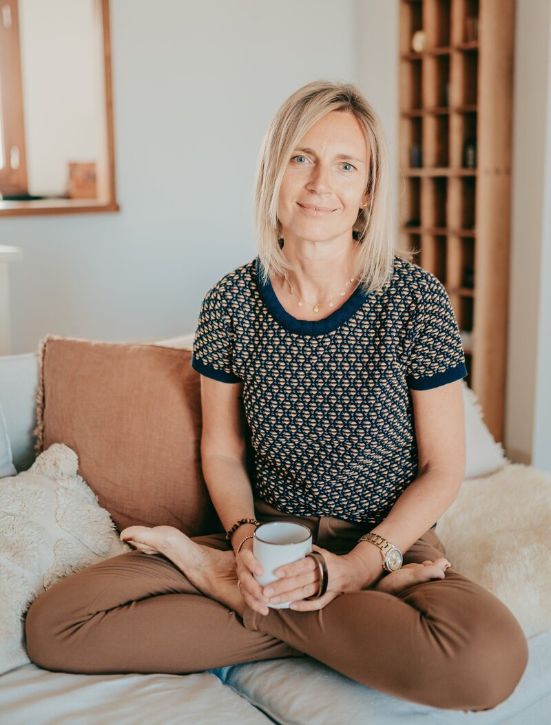 Sylke entspannt lächelnd mit einer Tasse Tee auf dem Sofa sitzend