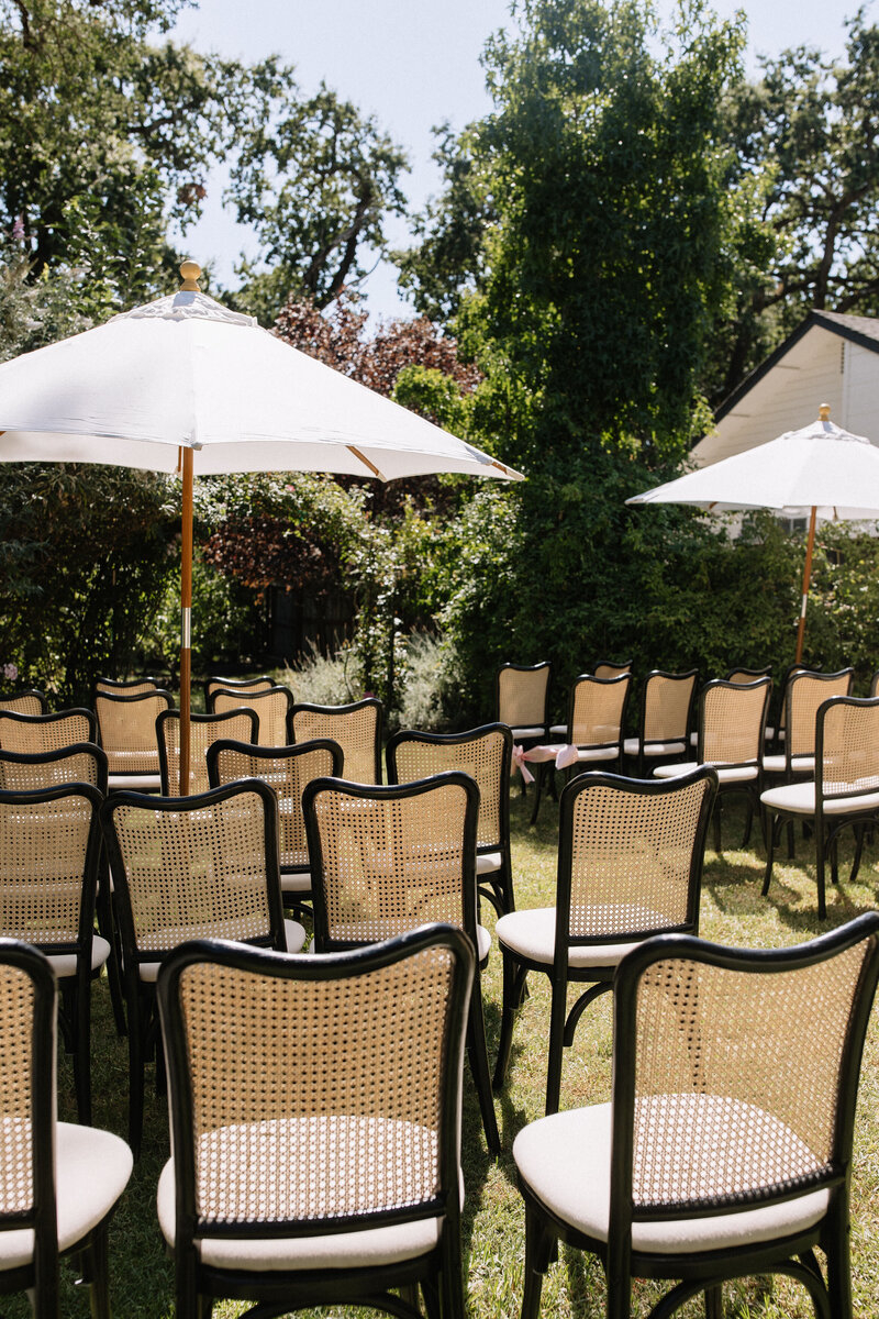 Outdoor garden wedding ceremony in Napa California with wicker and black chairs under white umbrellas