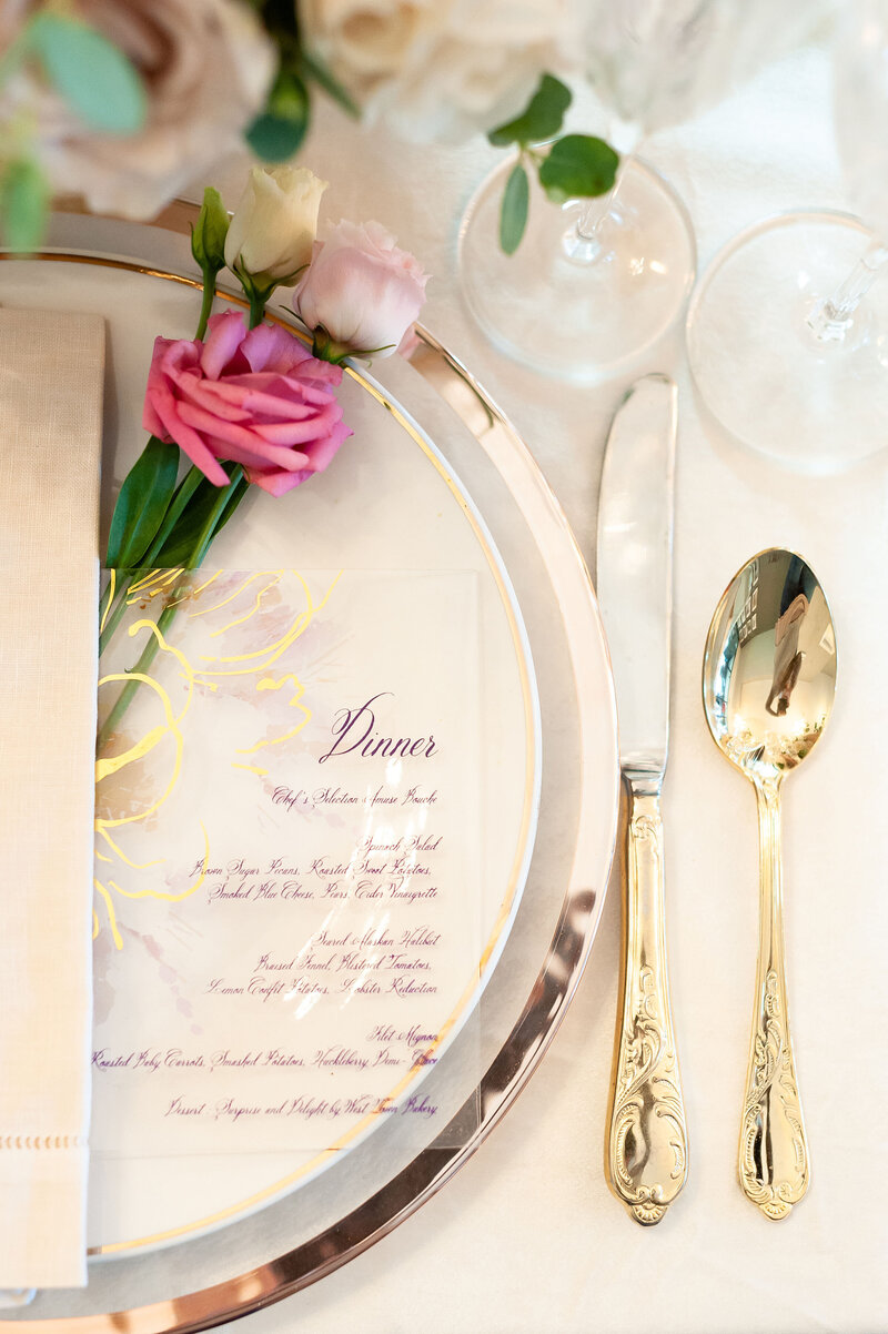 Chic wedding place setting with a gold-rimmed menu and fresh floral detail at a luxury event.