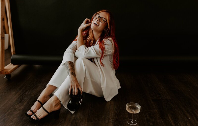 woman sitting on the ground in a white blazer suit holding a camera