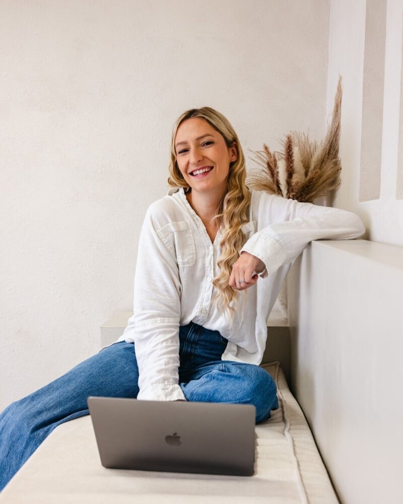 Giselle from The Lovers Passport sitting with her influencer coach laptop wearing jeans